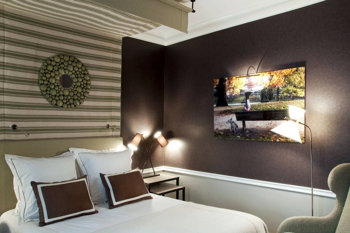 Une chambre d’hôtel avec un lit, des oreillers, une lampe, un tableau accroché au mur et un mur à rayures.