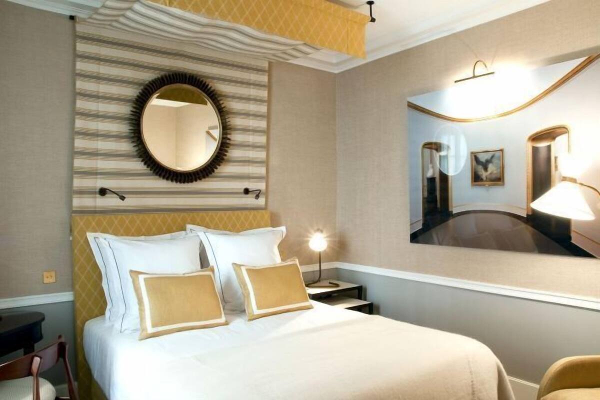 Une chambre d’hôtel comprenant un lit, une table de chevet, une lampe, un miroir et un miroir rond fixé au mur.