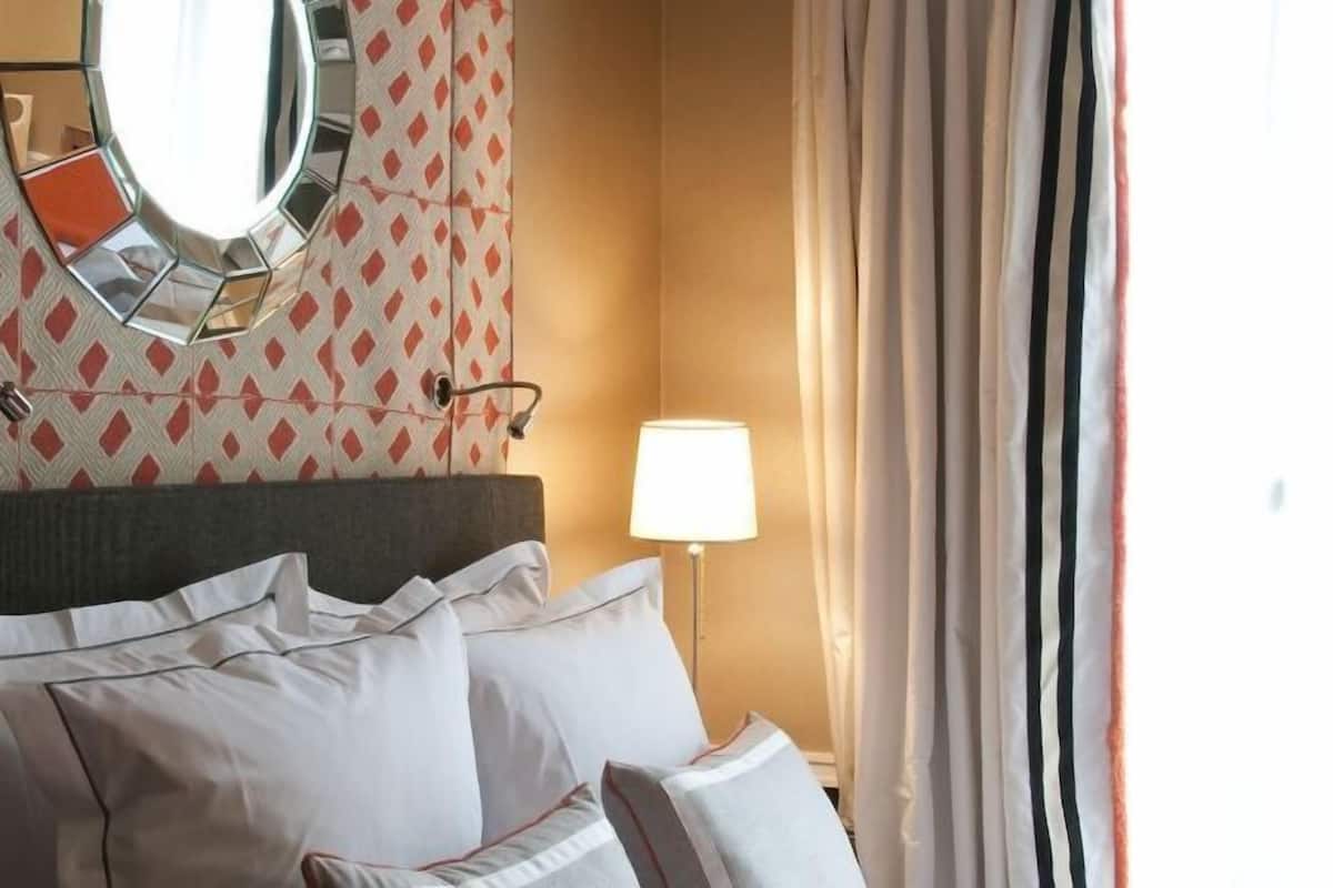 Une chambre d’hôtel avec un lit, des oreillers, une lampe de chevet, un miroir et des rideaux.