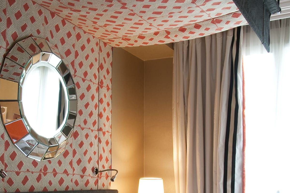 Une chambre d’hôtel avec un grand lit, un miroir rond, une lampe fixée au mur et des rideaux.