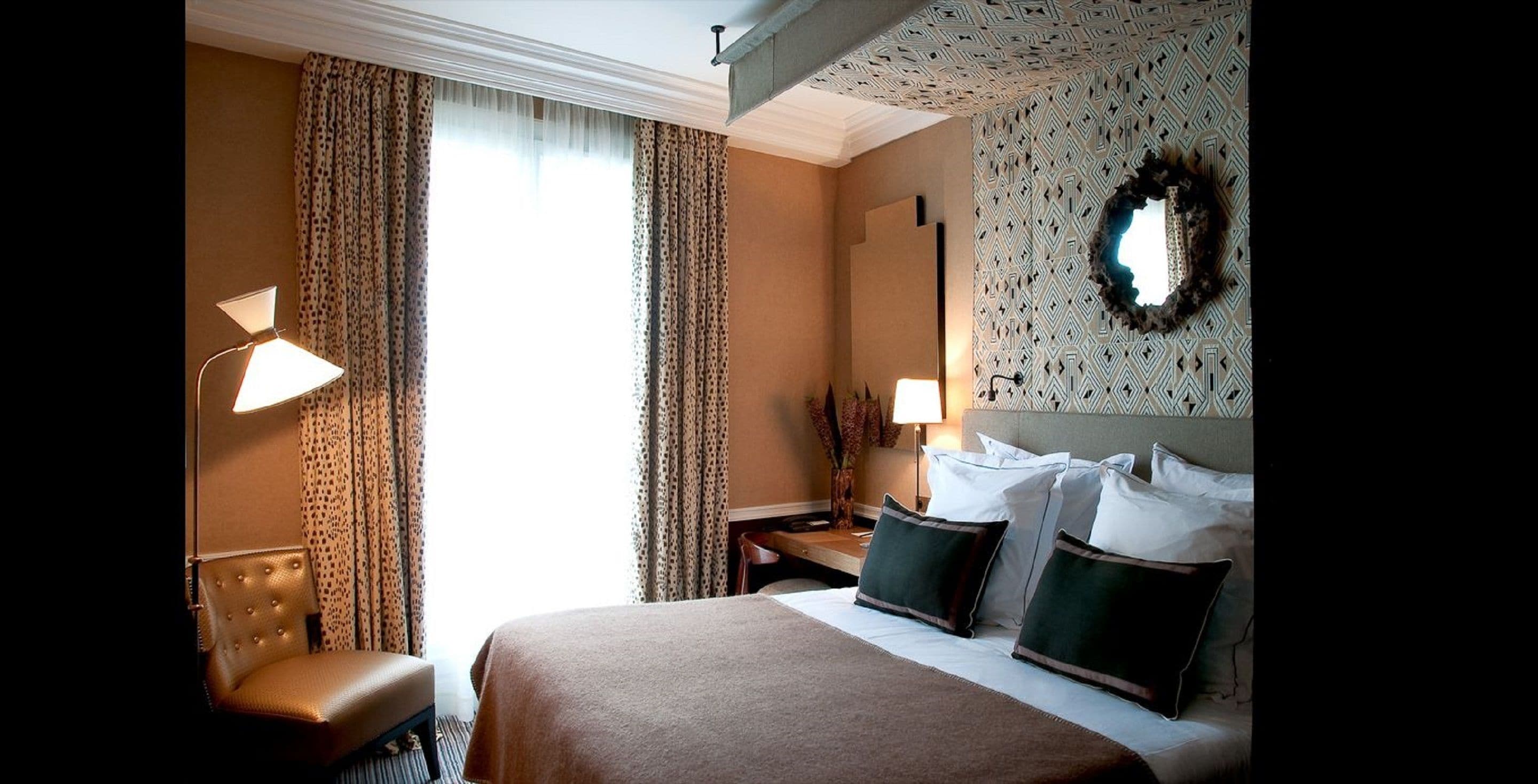 Una habitación de hotel con una cama grande, dos lámparas de noche, una silla, una mesita de noche y un papel tapiz decorado.