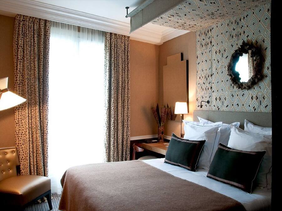 Una habitación de hotel con una cama grande, dos lámparas de noche, una silla, una mesita de noche y un papel tapiz decorado.