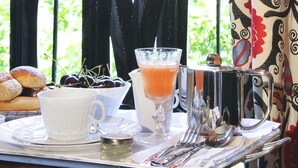 Una mesa dispuesta con alimentos para el desayuno, una bebida y un mug de plata, con vistas a un edificio con columnas.