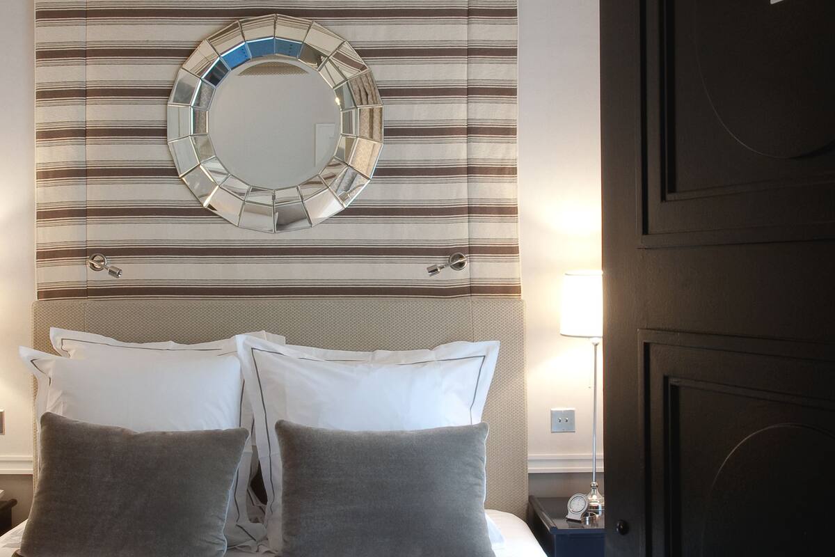 Une chambre d’hôtel avec un lit, un miroir rond, des rideaux à rayures et une porte portant le numéro 34.