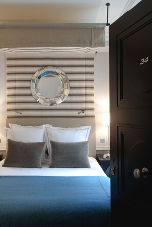 A hotel room with a bed, a circular mirror, striped curtains, and a door with the number 34. - Hotel Recamier (Paris)