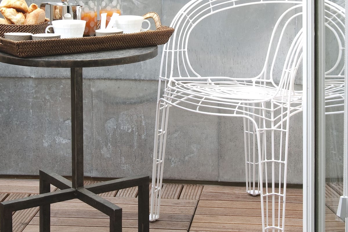 Un espace extérieur moderne, aménagé avec une table ronde, un panier en osier et des chaises en métal.
