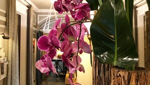 Un pasillo con una gran planta de orquídea en una maceta de madera, suelo a cuadros y un candelabro.