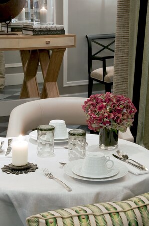 A dining table set with white plates, a cup, a candle, and a vase of pink flowers. - Hotel Recamier (Paris)