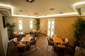 A dining area with wooden flooring, wicker chairs, and tables. There are potted plants and a television mounted on the wall. - Diufain (Conil de la Frontera)