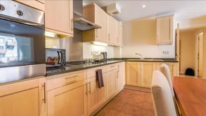 A compact kitchen with a Bosch oven, a microwave, and a sink. There is a dining table with chairs and a tiled floor. - London Tower Bridge Apartments (London)