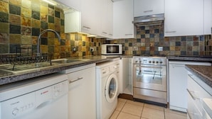 A compact kitchen with white cabinets, a dishwasher, a washing machine, a microwave, and a stainless steel oven. - London Tower Bridge Apartments (London)