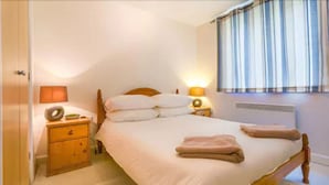 A bedroom with a bed, two bedside tables, a nightstand, a lamp, and a window with curtains. - London Tower Bridge Apartments (London)
