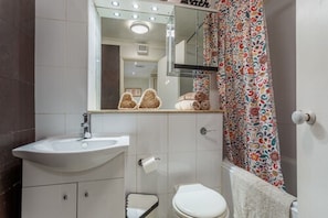 A bathroom with a white sink, a toilet, a mirror, and a shower curtain with a floral pattern.