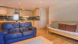 A modern living room with a blue leather sofa and a wooden coffee table. There is a kitchen area with white cabinets and a built-in oven. - London Tower Bridge Apartments (London)