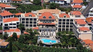 Un hotel con una piscina central rodeada de abundante vegetación y varios edificios con tejados rojos.