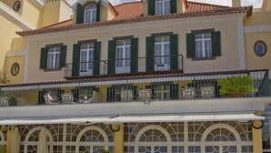 Un edificio con un área de café en terraza, con mesas al aire libre y una sección cubierta con grandes ventanales.