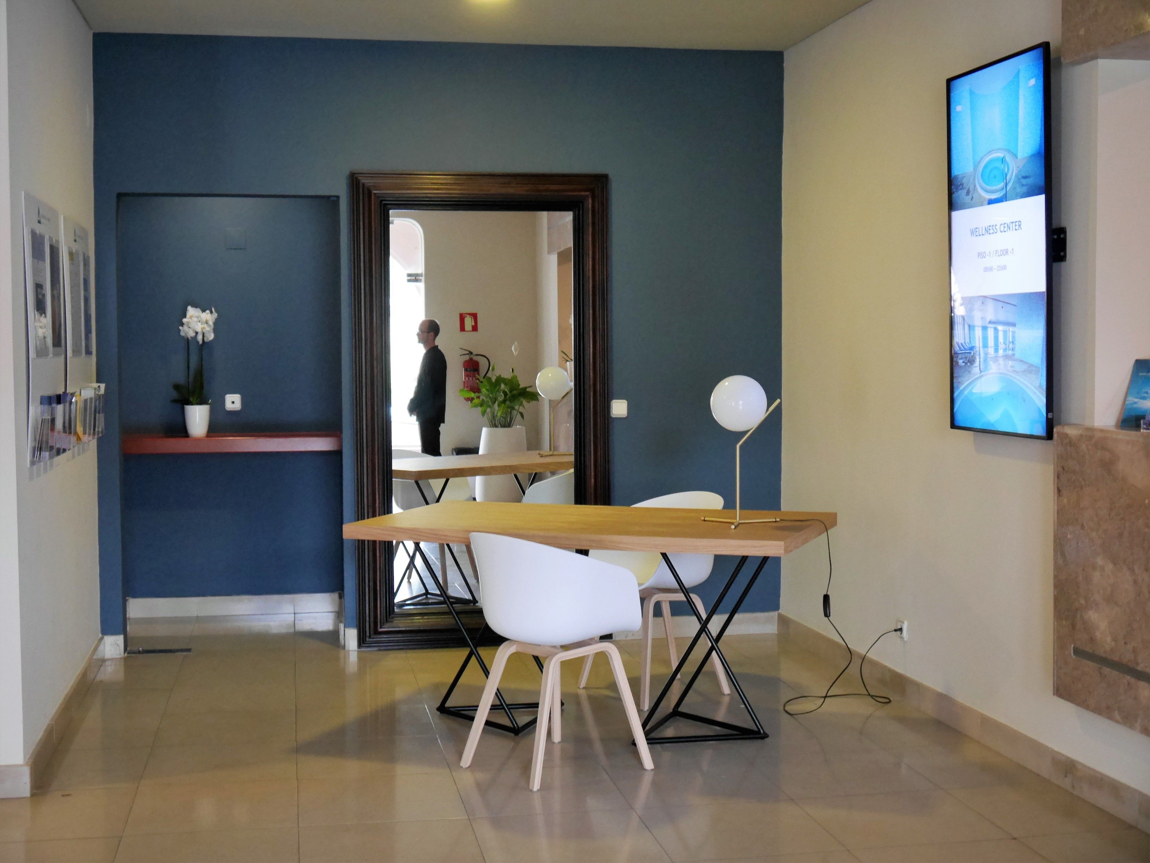 Un espace de bureau moderne avec une table en bois, des chaises blanches, une plante en pot et un tableau encadré au mur.