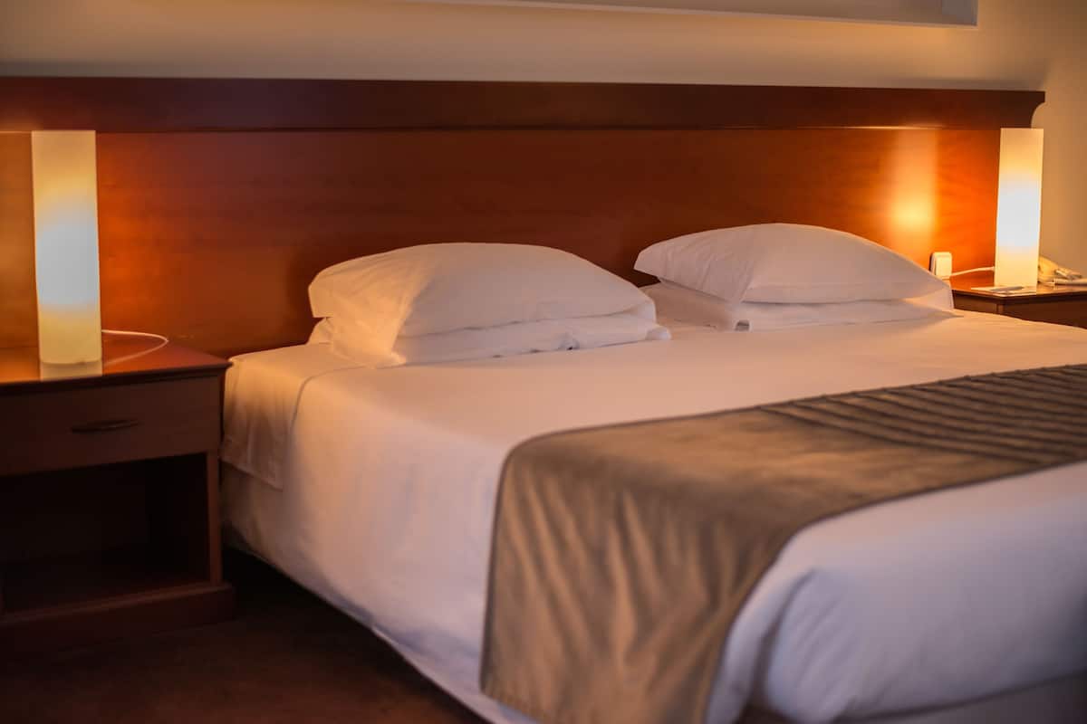 A hotel room with a wooden headboard, two white pillows, a neatly made bed, and bedside lamps.
