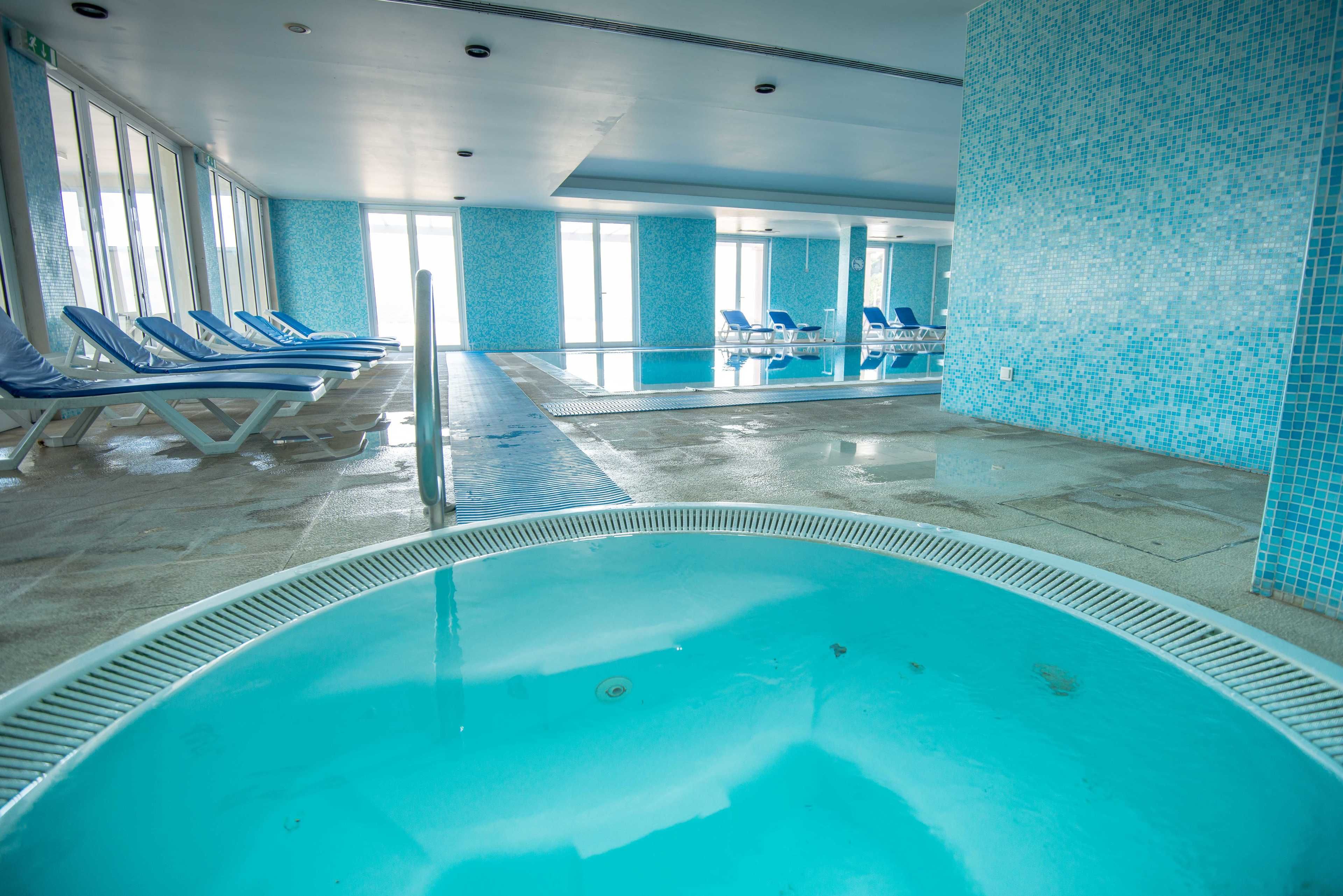 Piscina interna com paredes azulejadas em azul e vista clara da área da piscina.