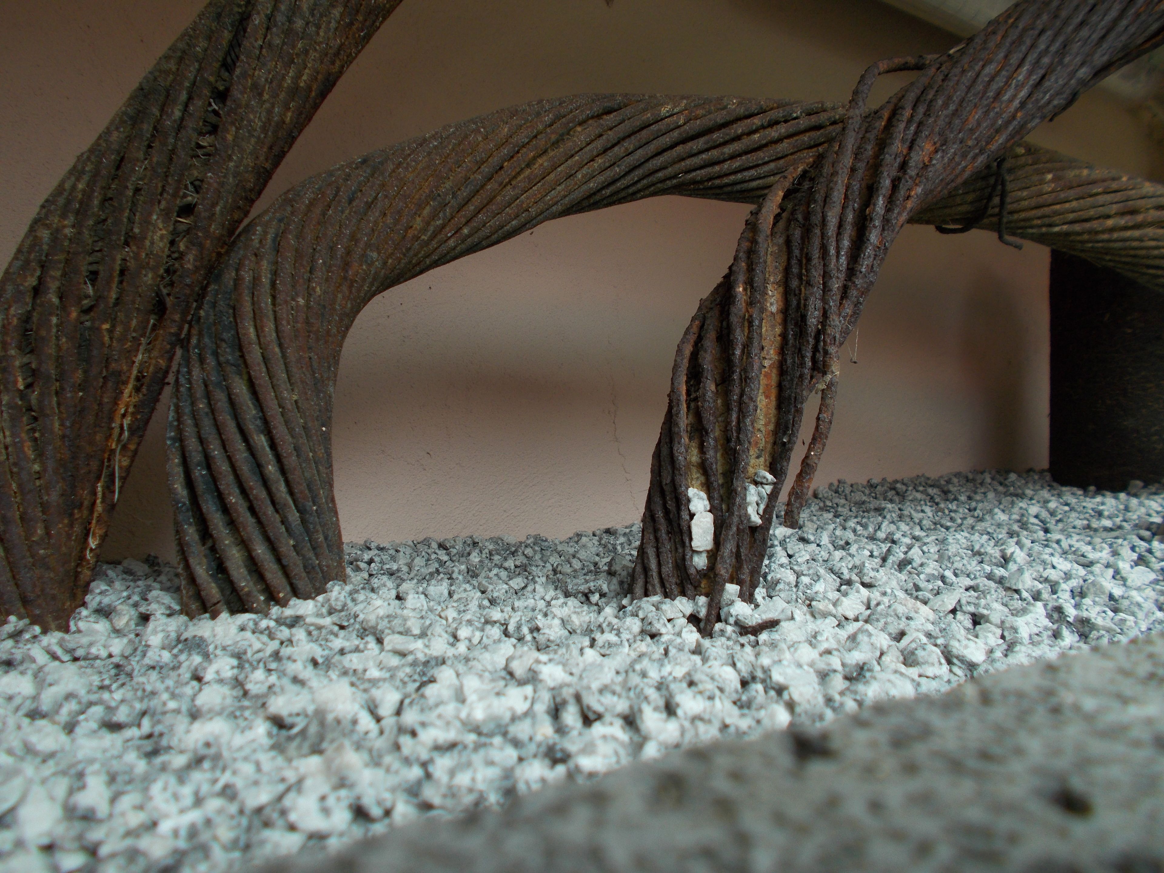 Ein Detailaufnahme von verdrehten Metallstangen mit rauer Oberfläche vor schlichtem Hintergrund.