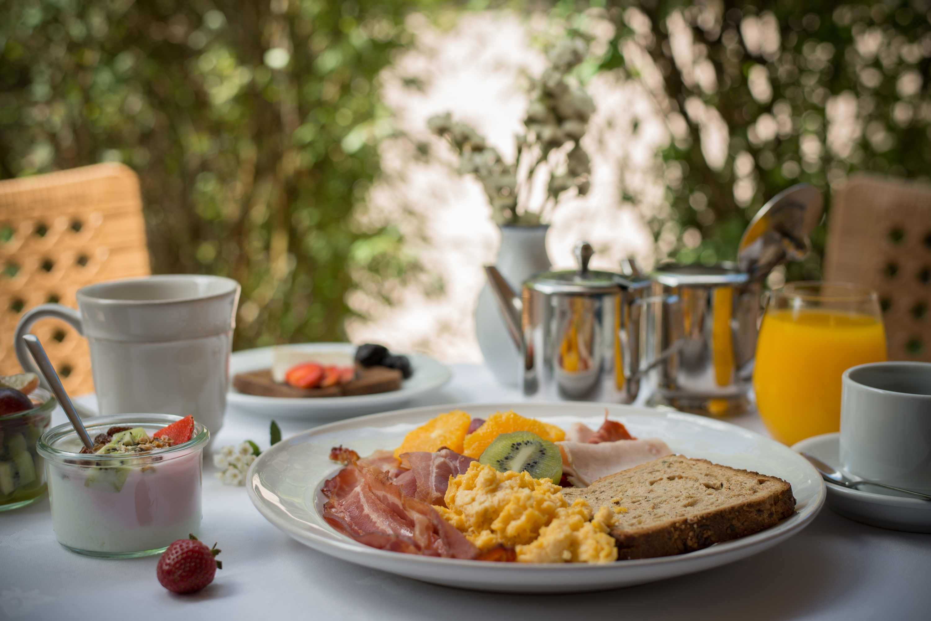 A breakfast table with various food items, a jug, a cup, and a glass of orange juice.