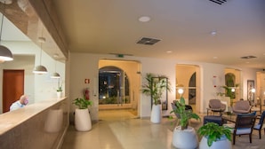 Un hall de hotel con mostrador de recepción, zona de estar y plantas en macetas.