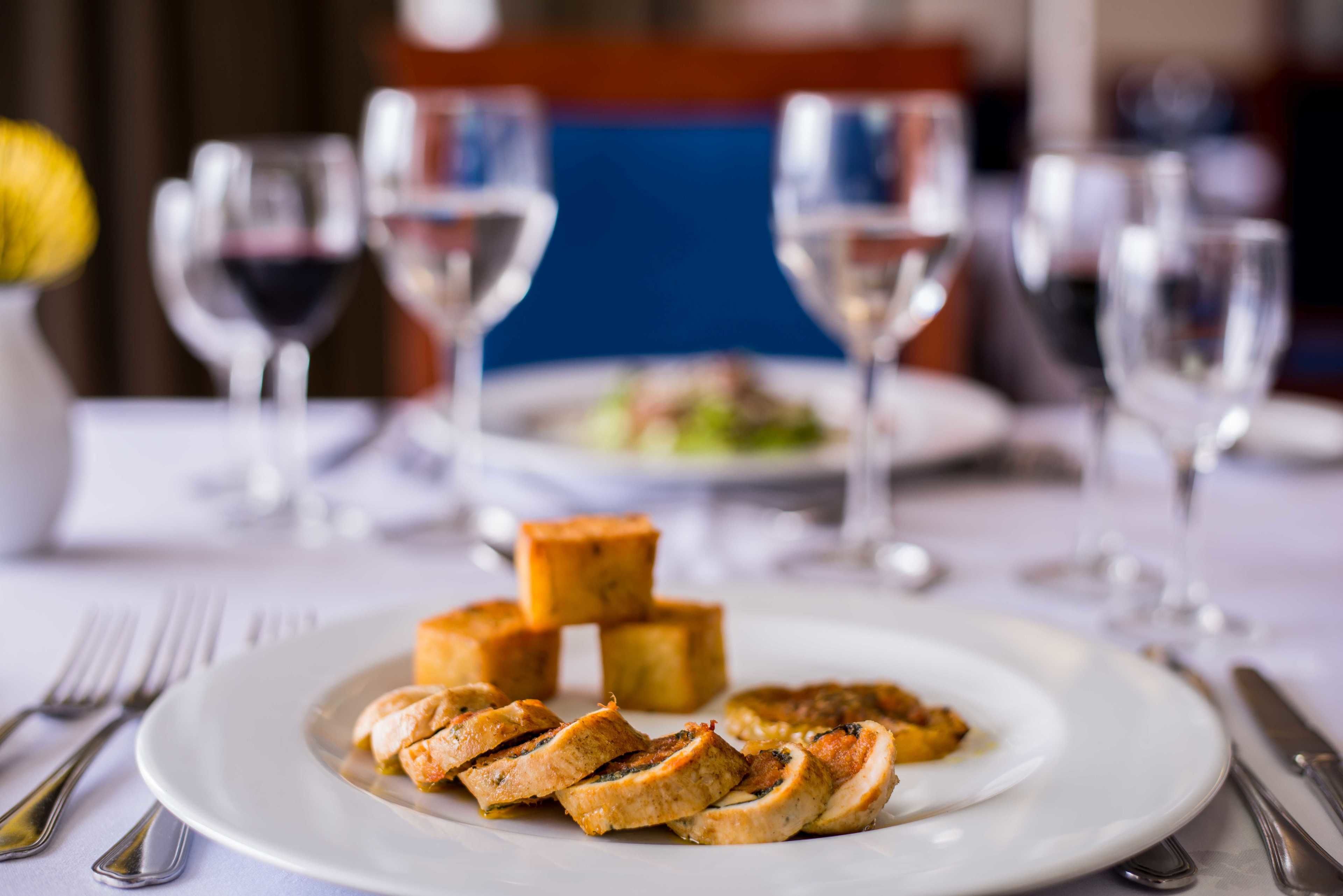 A dining table with a plate of food, wine glasses, and cutlery.