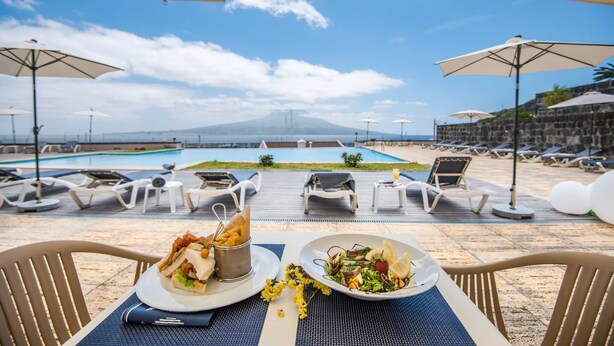 Un área de comedor con vista a la piscina, mobiliario exterior y una montaña al fondo.