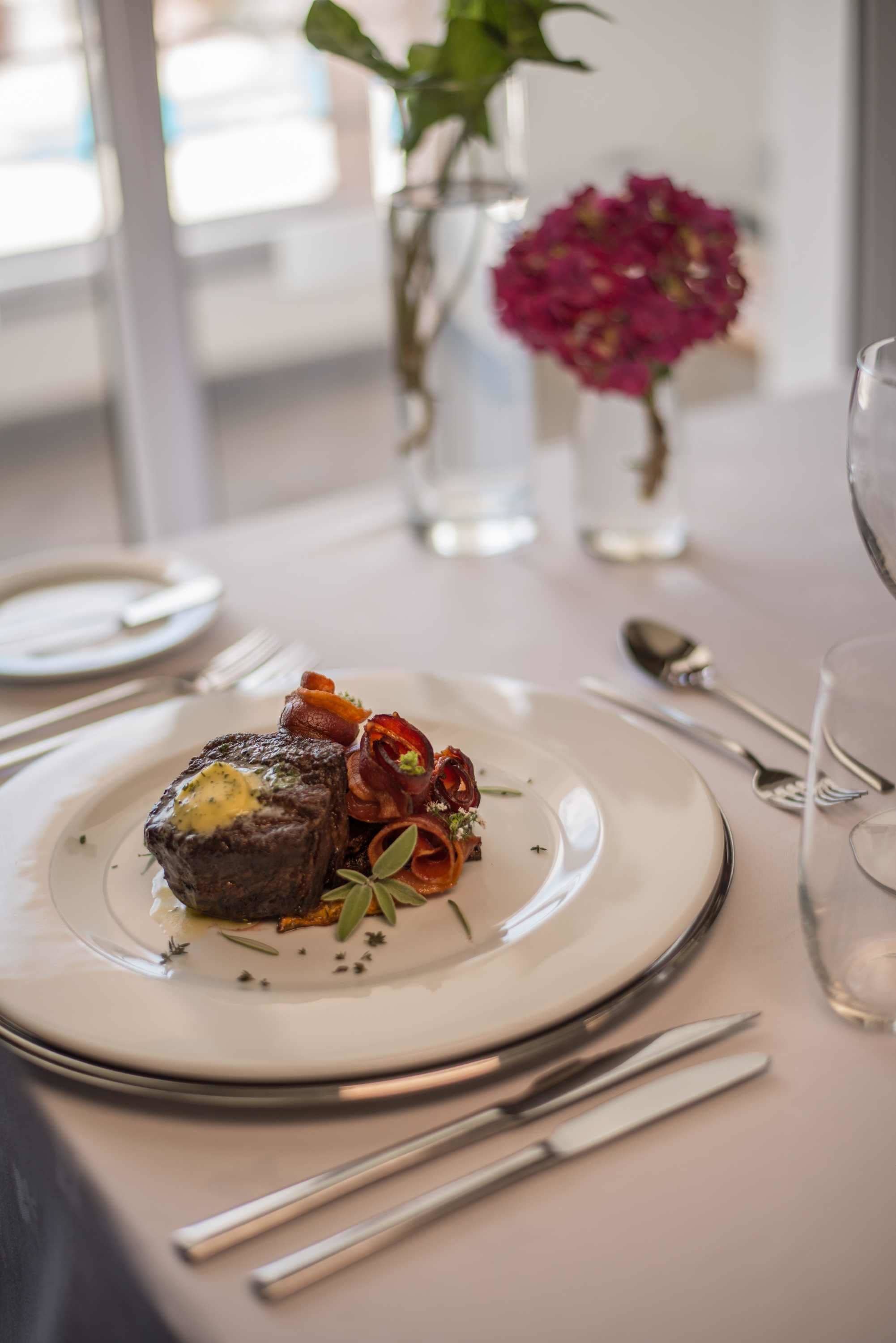 A plate of food with a steak, vegetables, and a small vase with flowers.
