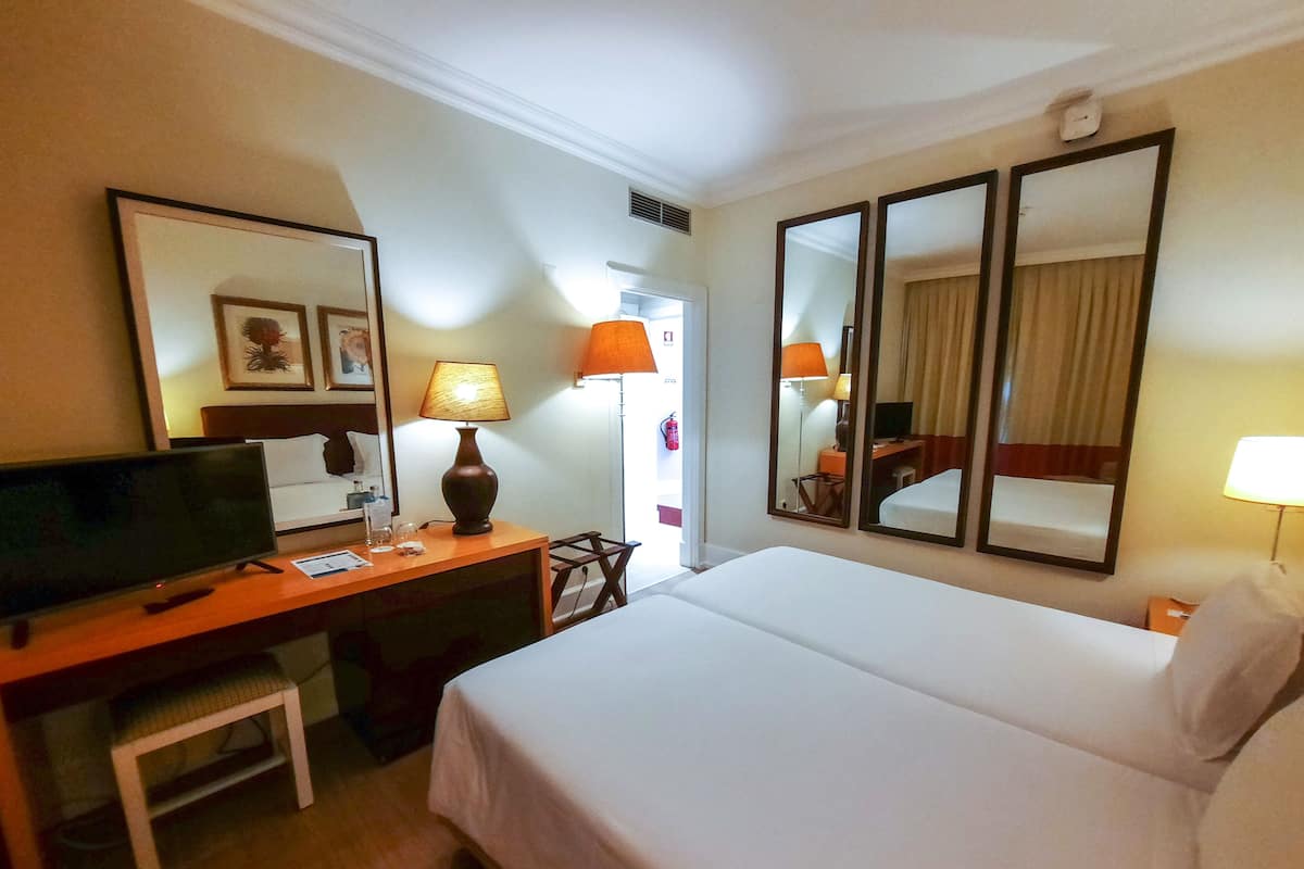 A hotel room with a bed, desk, television, lamps, and mirrors.
