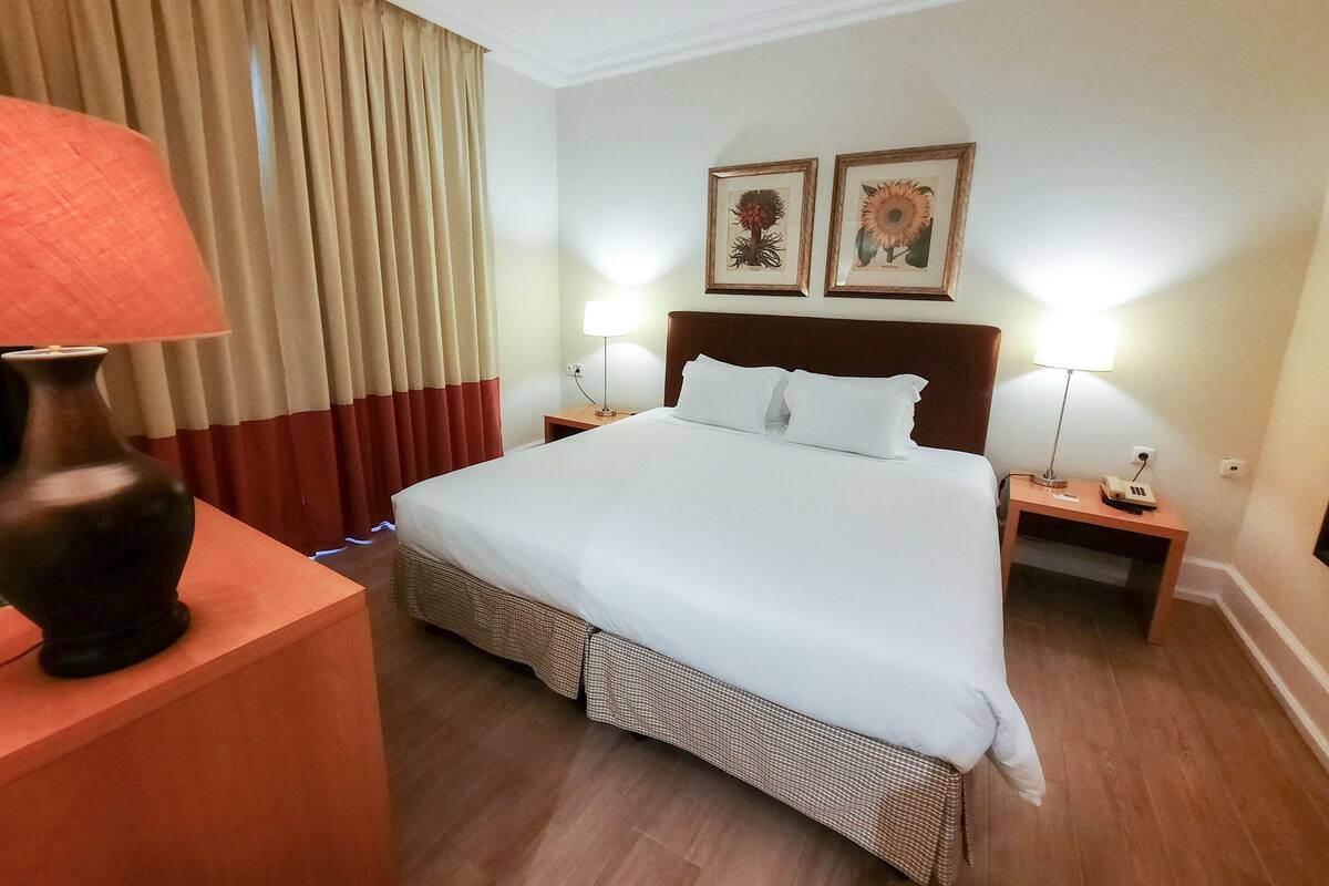 A hotel room with a large bed, two bedside tables, a lamp, and a vase.