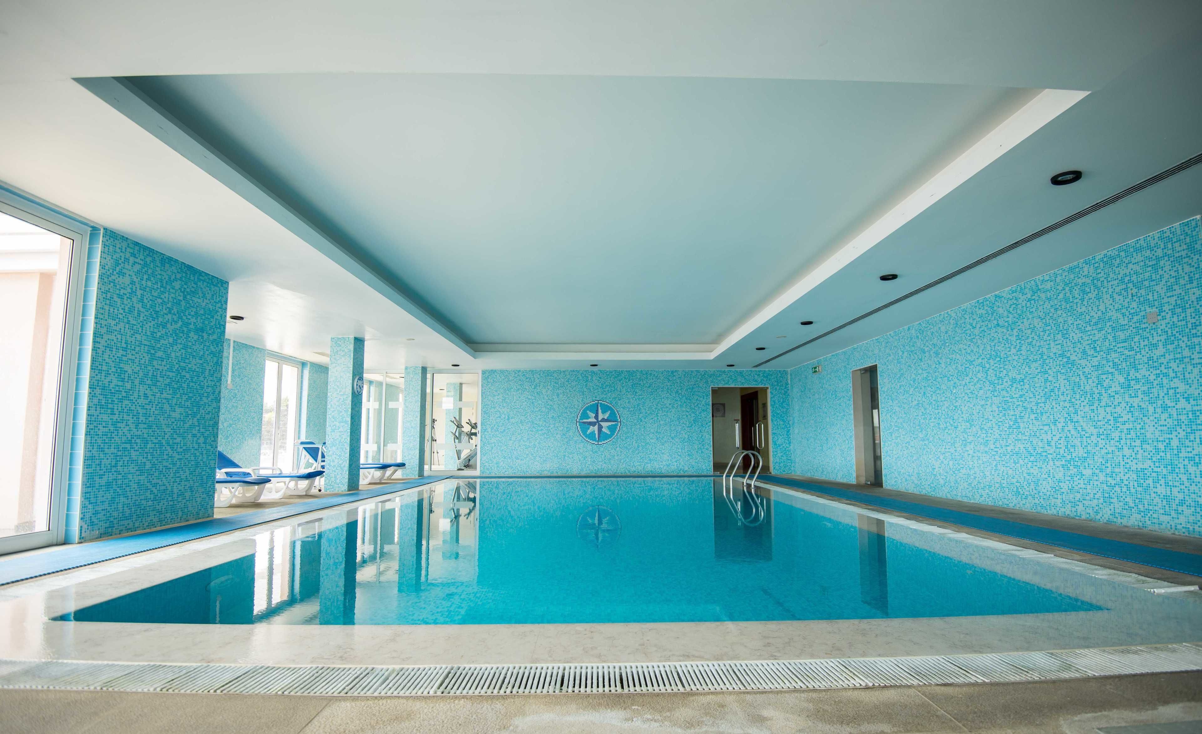 Una amplia piscina interior con paredes de mosaicos azules y base de vidrio transparente.