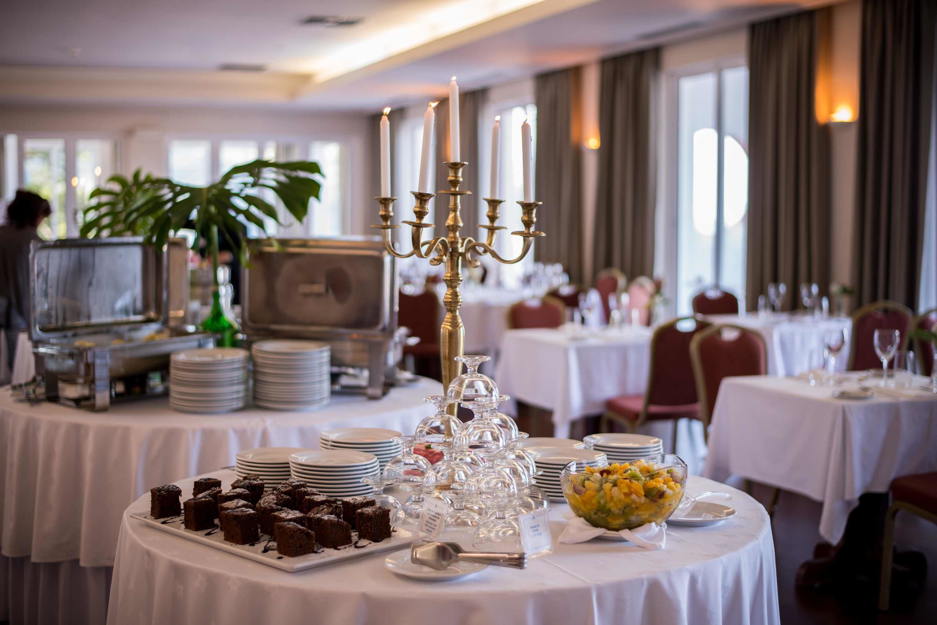 A dining area with round tables set for a meal, featuring a candelabra centerpiece, dessert plates, and a fruit bowl.