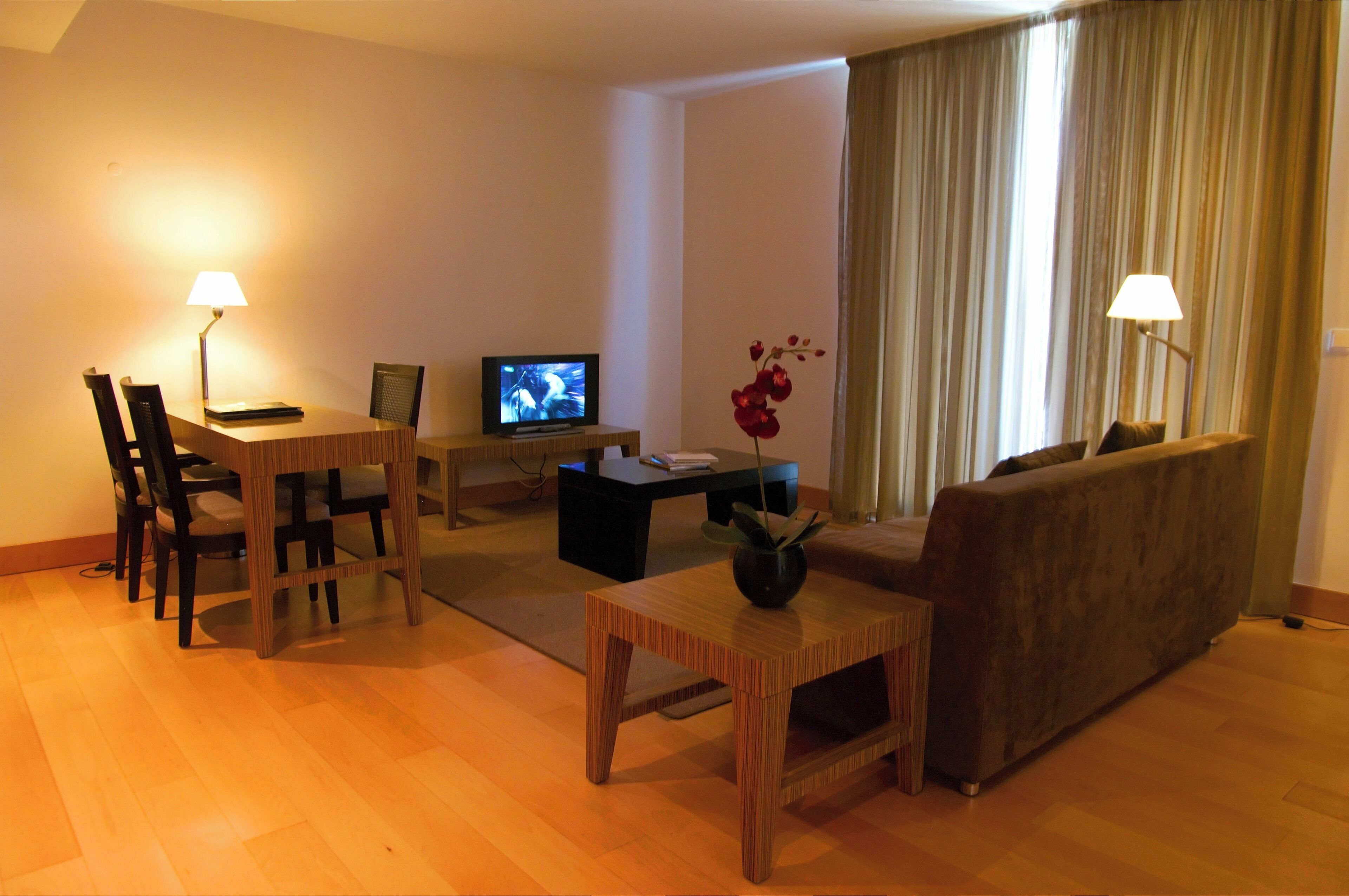 A living room with a wooden dining table, chairs, a sofa, a coffee table, and a TV on a stand.