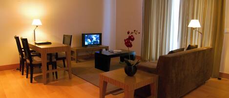 Una sala de estar con una mesa de comedor de madera, sillas, un sofá, una mesa baja y un televisor sobre un mueble.