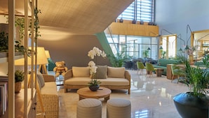 A spacious lobby with a high ceiling, a sofa, chairs, a coffee table, and potted plants. - Golden Residence Hotel (Funchal)