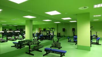 Ein Fitnessstudio mit Spiegelwänden, unterschiedlichen Trainingsgeräten und heller Beleuchtung.
