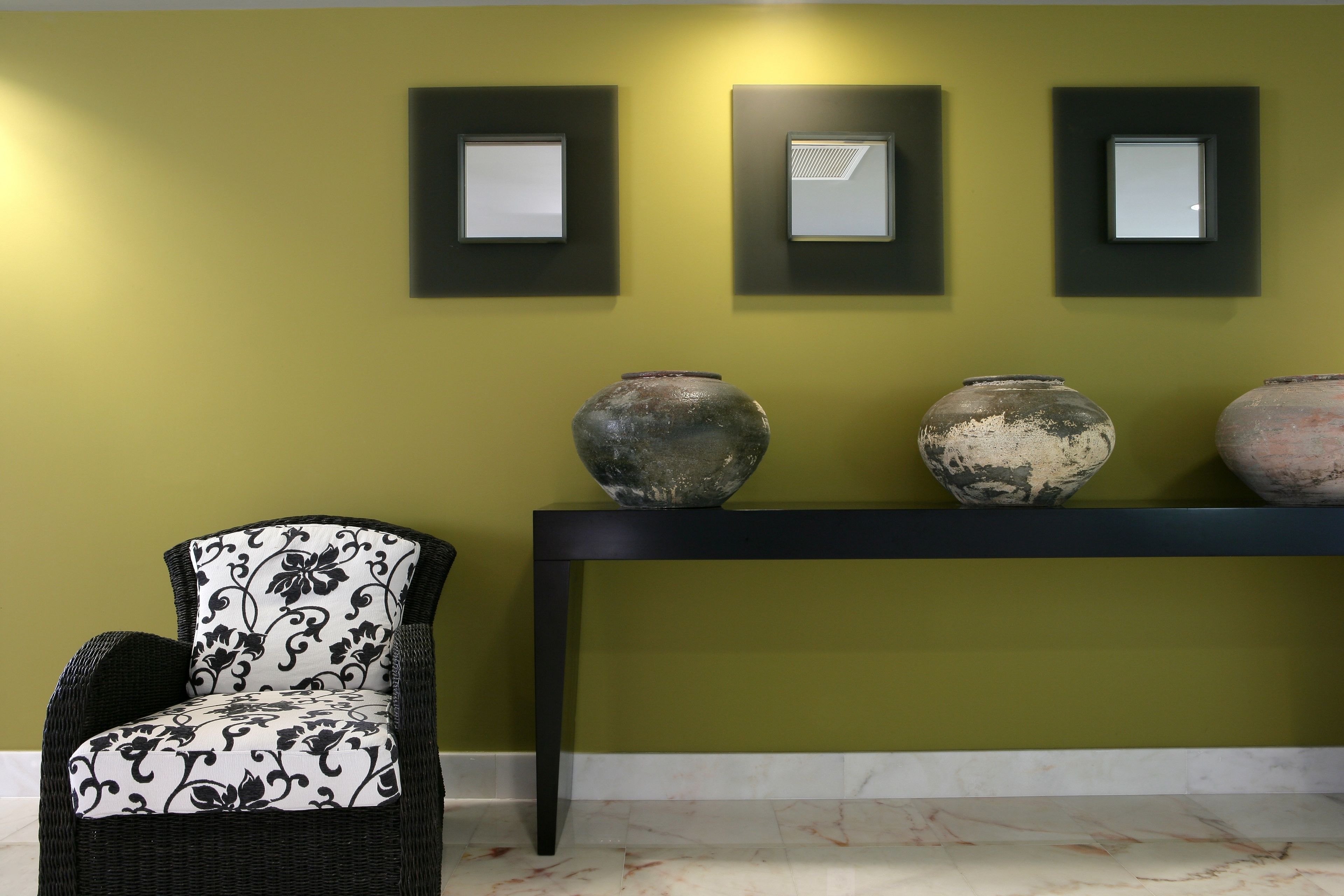 Una stanza con una parete verde, uno specchio con cornice nera e un tavolo con tre vasi.