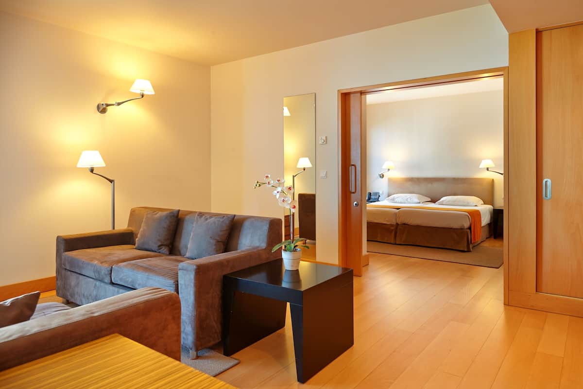 A modern hotel room with a sofa, a small table, a mirror, and a bed with a headboard.