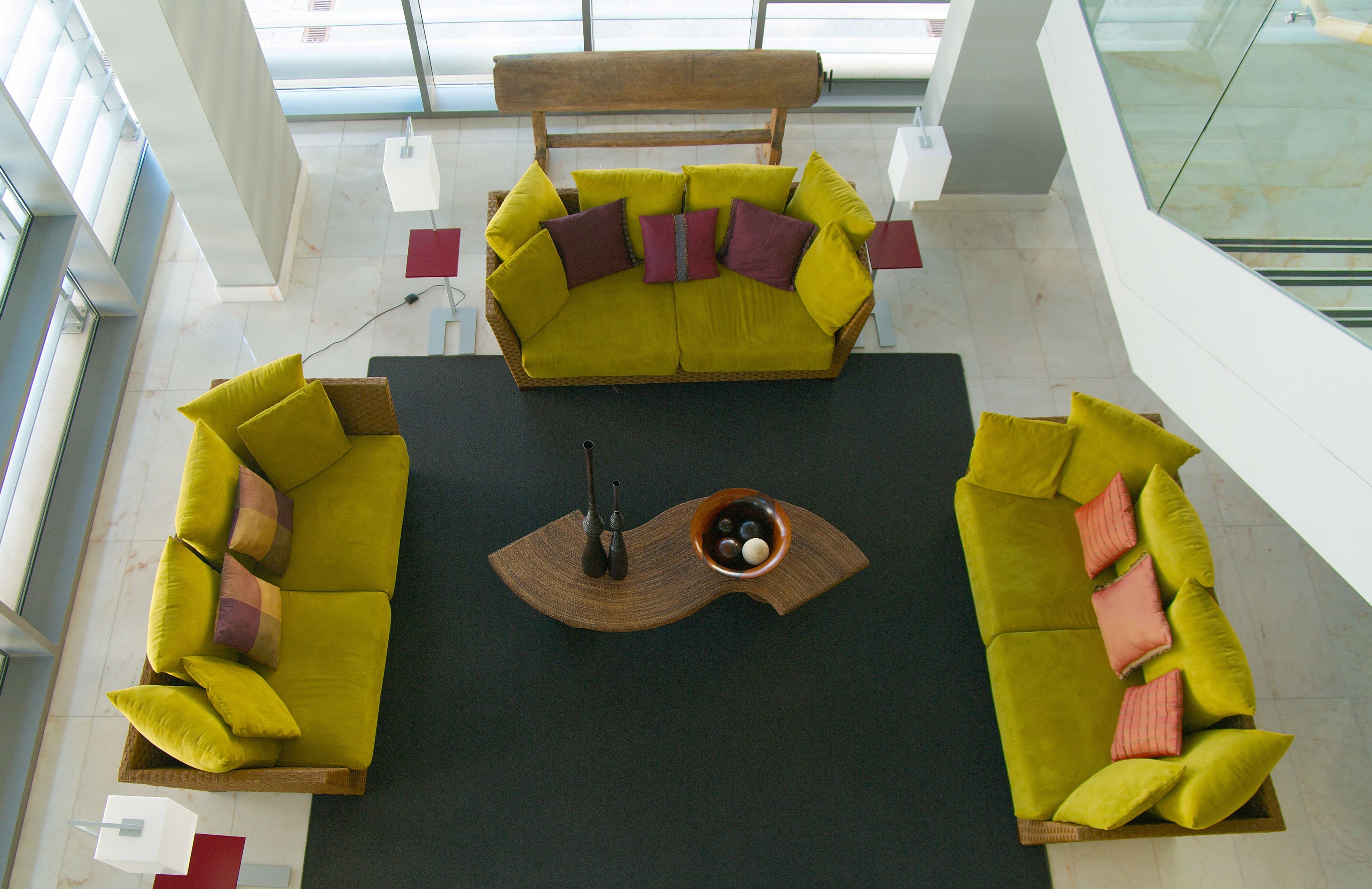 Un interior moderno con un tapete negro central, dos sofás verdes con cojines y una mesa de centro de madera con objetos decorativos.
