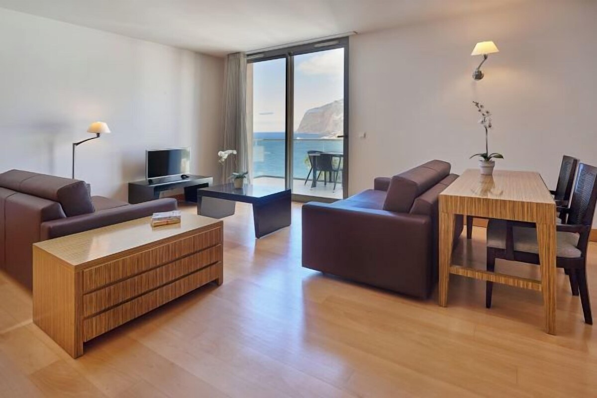 A modern living room with a sofa, coffee table, TV, and a dining area with a table and chairs.