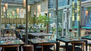 A modern restaurant with glass tables and chairs, indoor plants, and a view of the outdoors. - Golden Residence Hotel (Funchal)