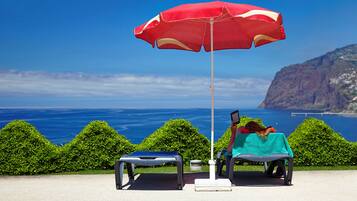 A beachside seating area with a red umbrella, a table, and a bench.