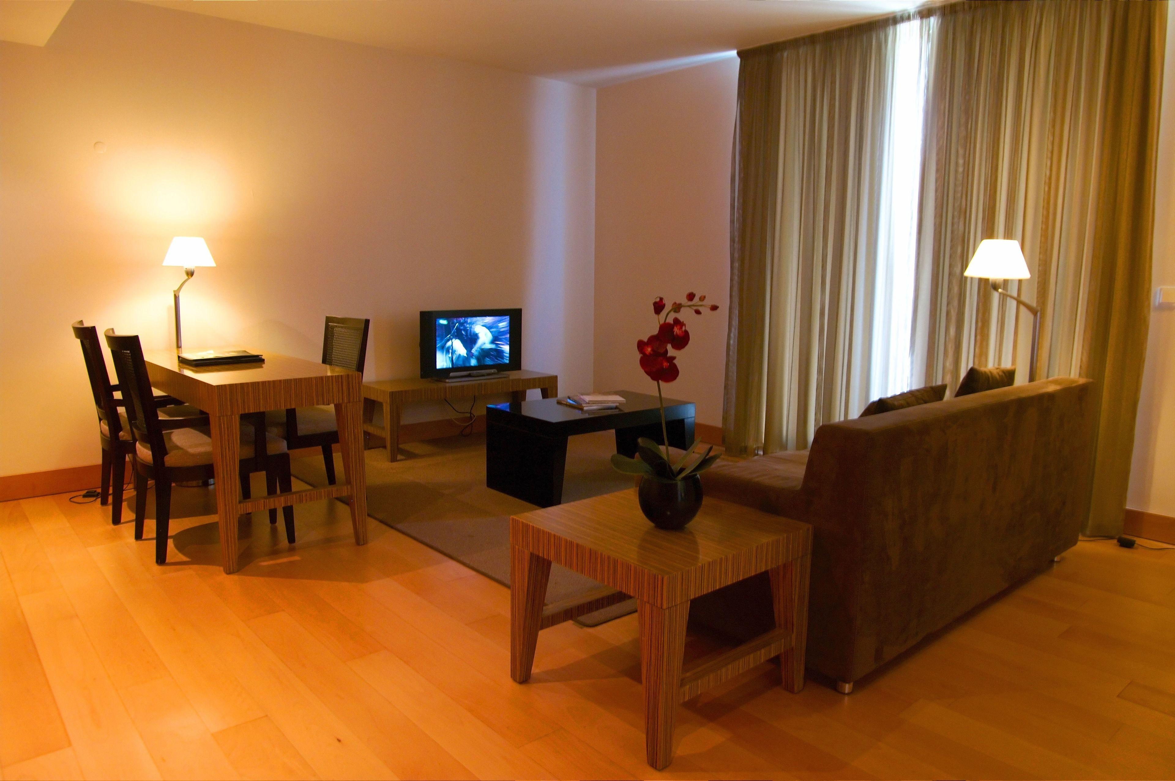A living room with a wooden table, a sofa, a TV, and two lamps.