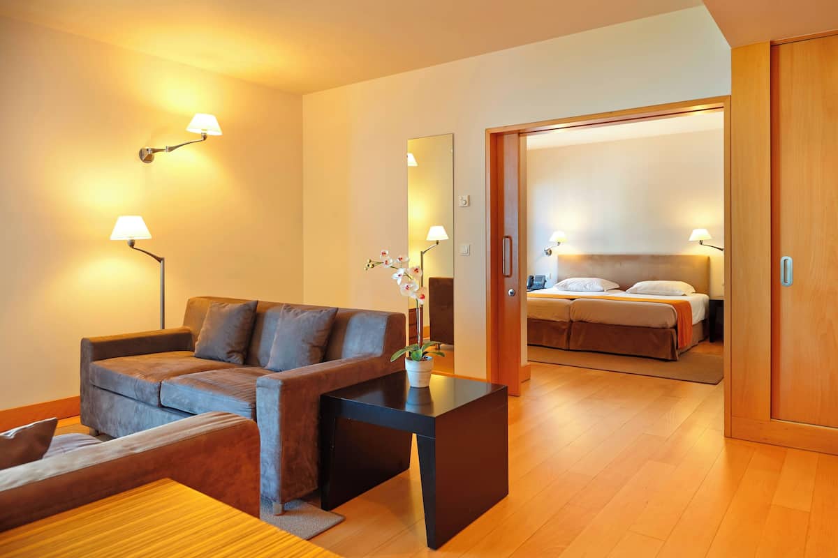 A modern hotel room with a sofa, a small table, a mirror, and a bed with a headboard.