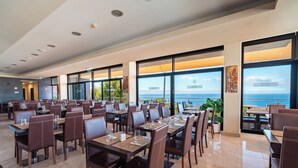 A spacious restaurant with multiple tables and chairs, large windows offering ocean views, and a clean, modern interior design. - Muthu Raga Madeira Hotel (Funchal)