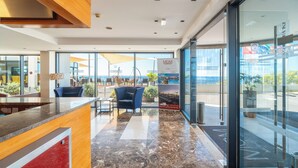 A modern hotel lobby with a reception desk, seating area, and large windows offering a view of the ocean. - Muthu Raga Madeira Hotel (Funchal)