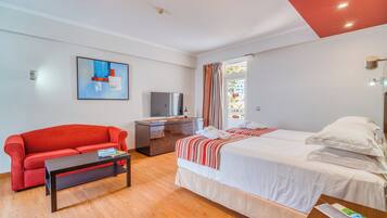A hotel room with a red sofa, a bed with white bedding, a wooden coffee table, a TV on a wooden cabinet, and a painting on the wall.