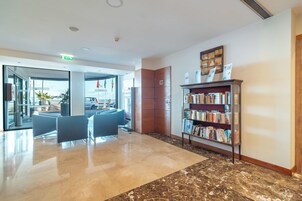 A modern lobby with a marble floor, a reception desk, a seating area, and a bookshelf.