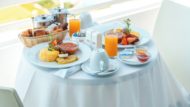 A breakfast table with a view of the ocean, a white tablecloth, and various breakfast items including eggs, toast, and orange juice. - Muthu Raga Madeira Hotel (Funchal)